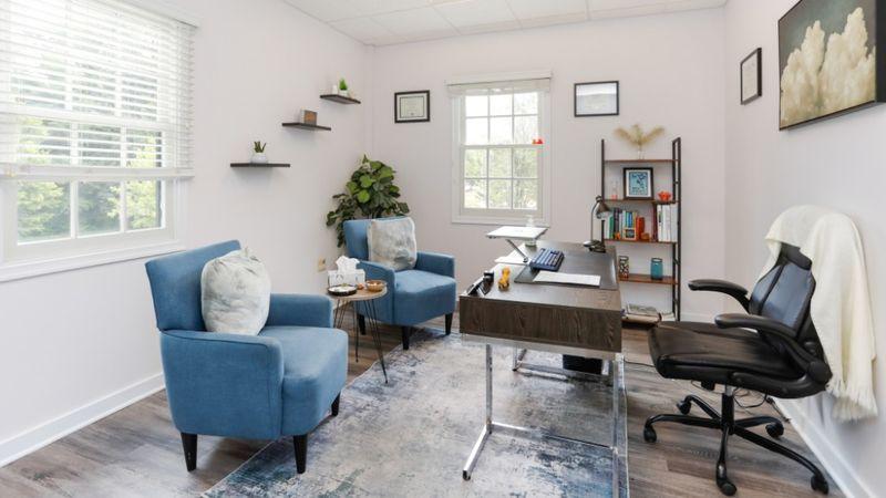 Therapist office at Rolling Hills Recovery Center with desk, blue chairs, bookshelves, and natural light.