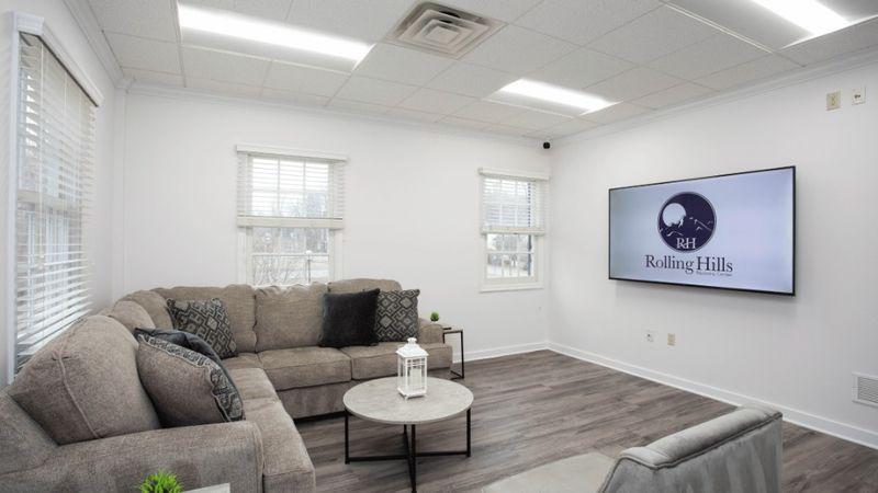 Client lounge with sectional sofa, coffee table, and large screen at Rolling Hills Recovery Center.
